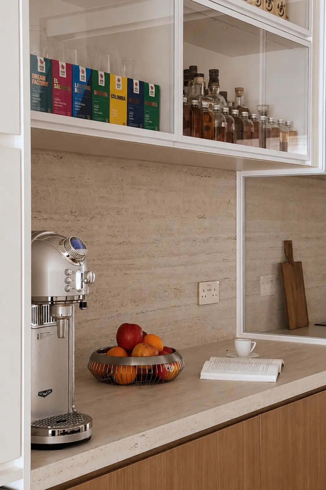 Minimalist dry kitchen with a glass display cabinet, travertine-inspired backsplash, and warm wood cabinetry.