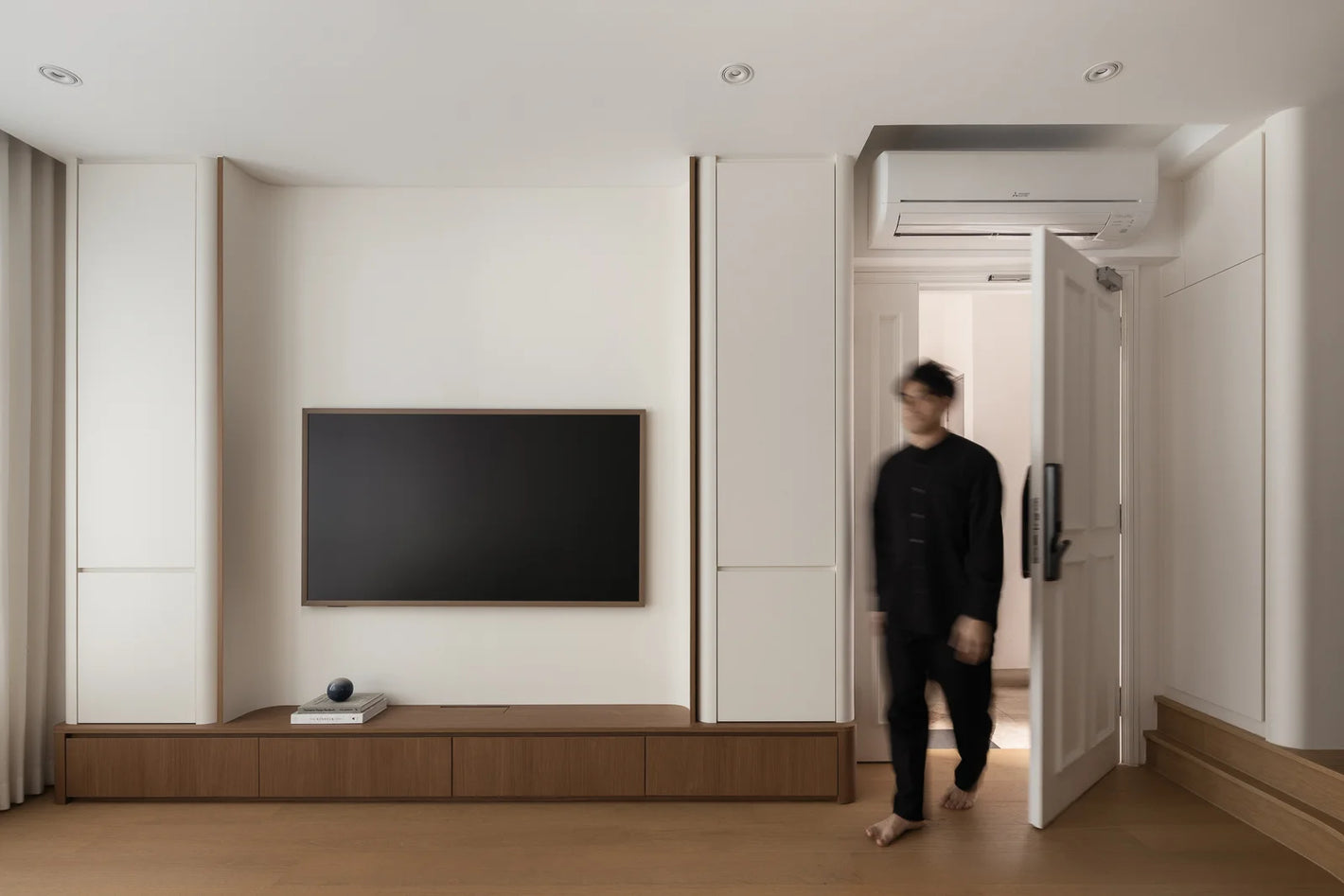 Minimalist living room with a curved TV feature wall as a person enters through the main entrance