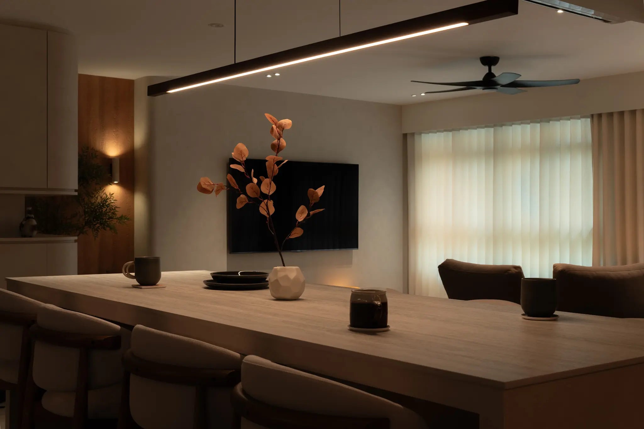 Modern kitchen island with upholstered chairs, a black linear pendant light and a wall-mounted TV in an open-plan living space